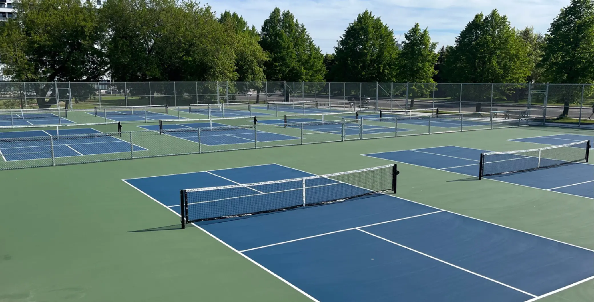 Toronto's new pickleball courts with 16 playing areas, surrounded by green trees and a clear sky, showcasing a modern sports facility.