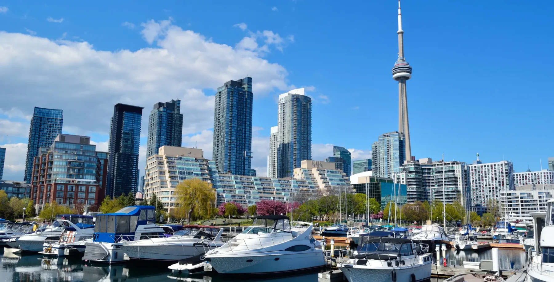 Toronto skyline with high-rise buildings and marina with boats, under a partly cloudy sky.