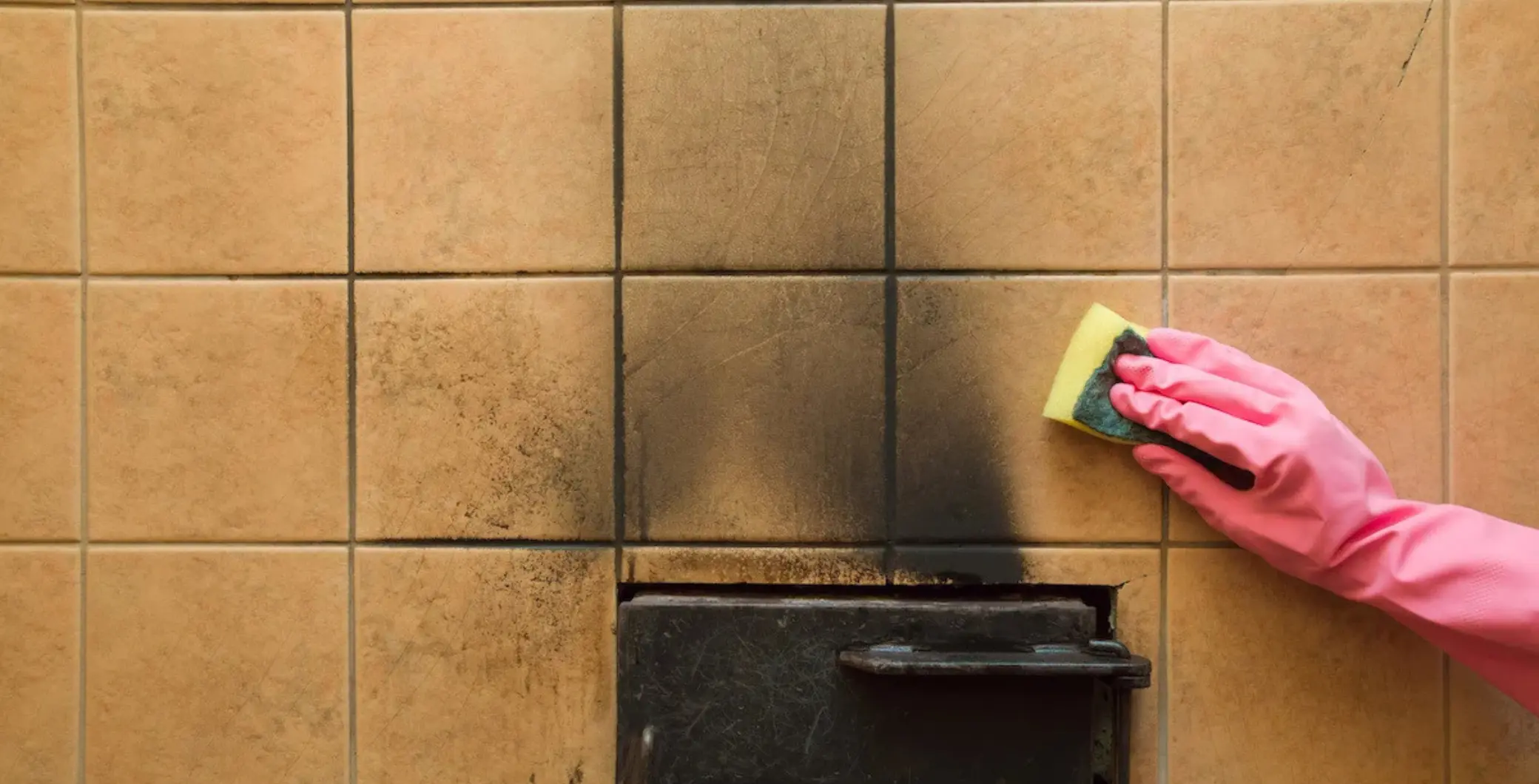 Person wearing pink gloves cleaning soot-stained wall tiles with a sponge, highlighting wildfire smoke residue concerns.