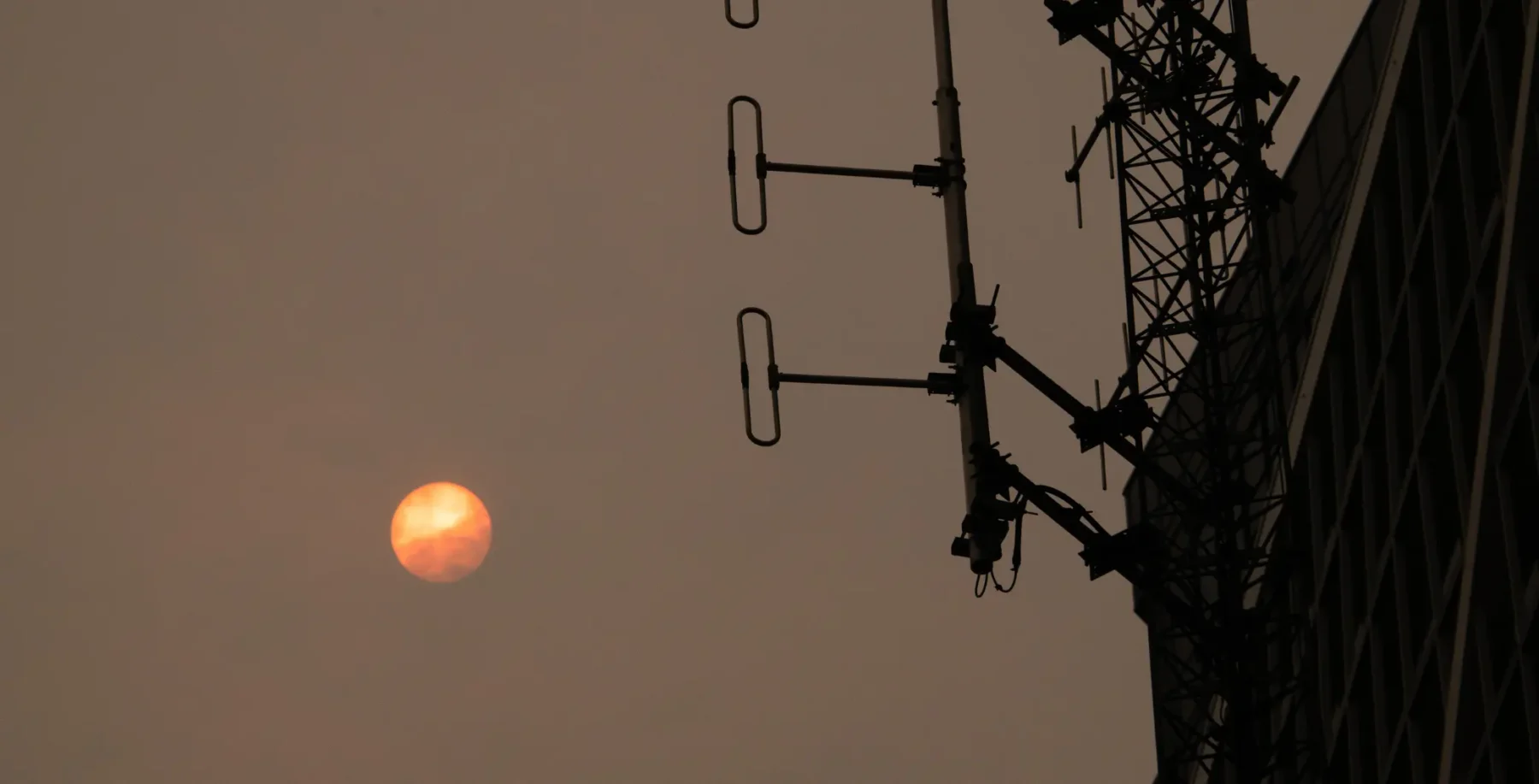 A large, reddish moon visible in the sky near a tall electrical tower with antennas, against a dusky, orange-tinted sky in Toronto.