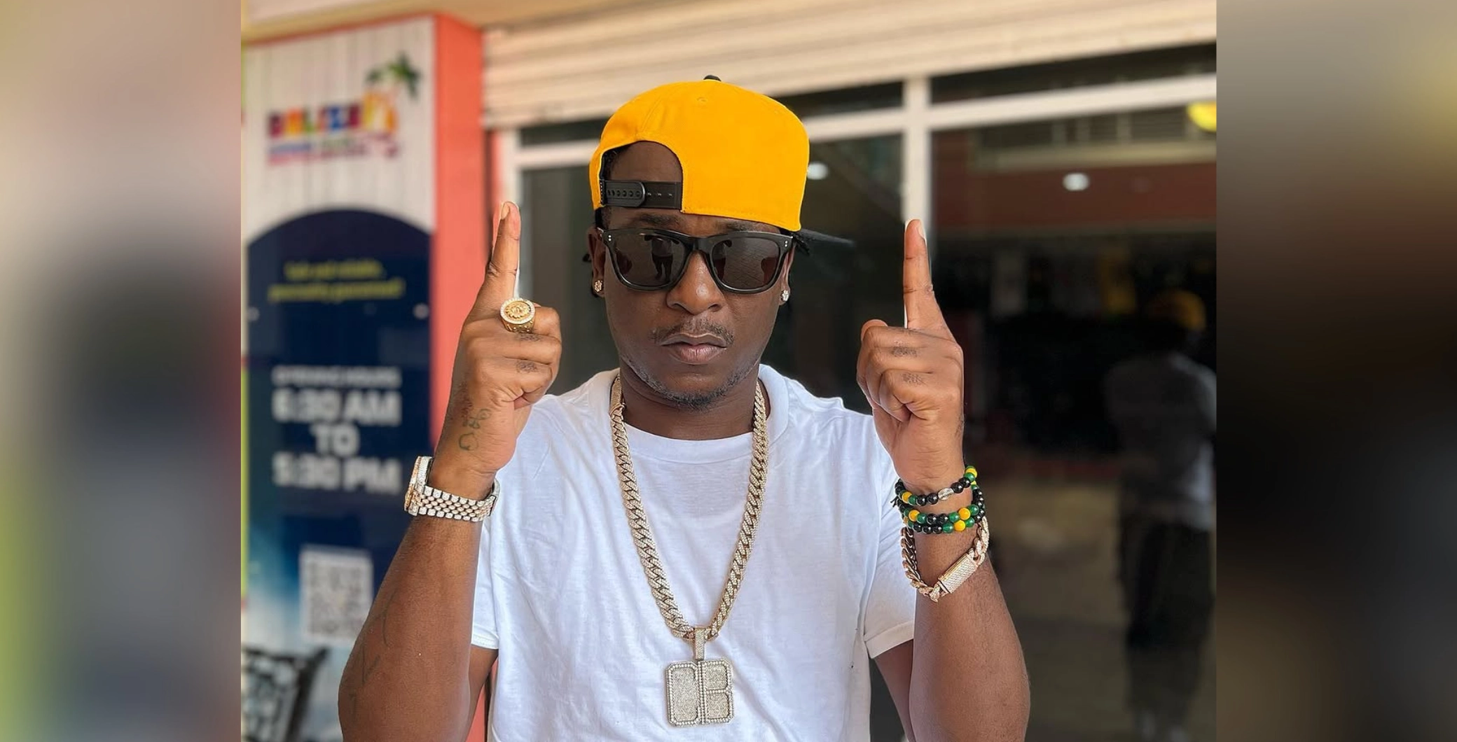 Charly Black, Jamaican dancehall artist, wearing a yellow cap, sunglasses, and jewelry, pointing upwards in Toronto for an upcoming show.