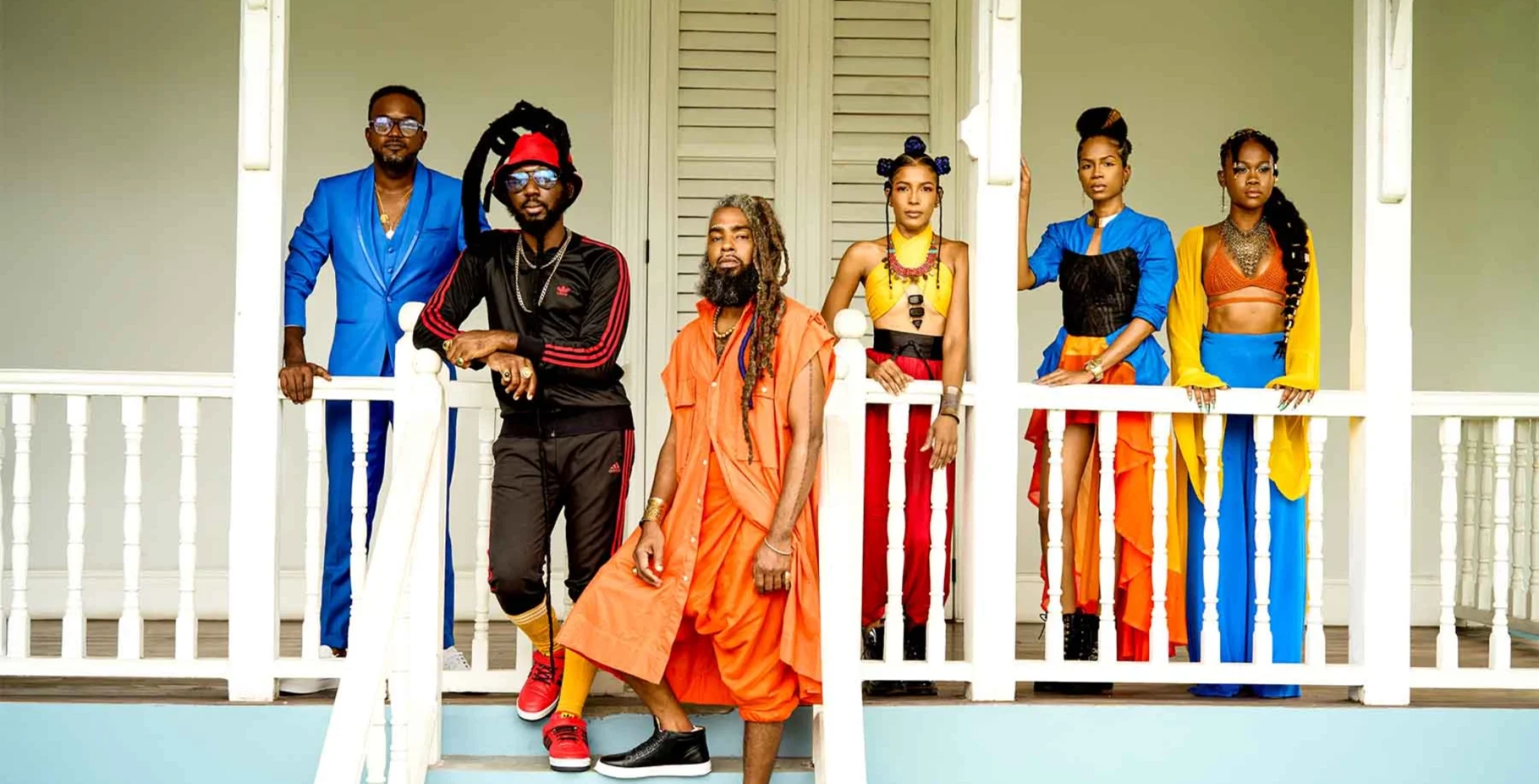 Trinidadian band members in colorful outfits on a porch, showcasing Caribbean culture and vibrant fashion.