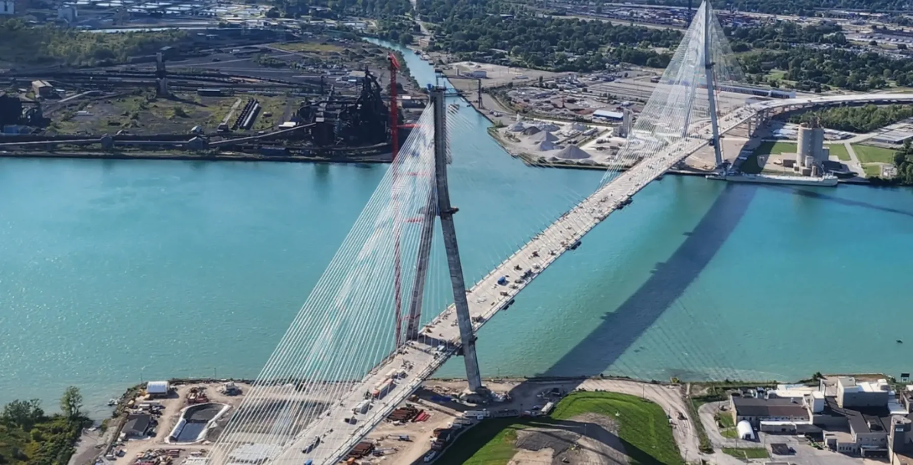 Aerial view of Canada's newest international bridge connecting two urban areas over a river, with construction and surrounding infrastructure visible.