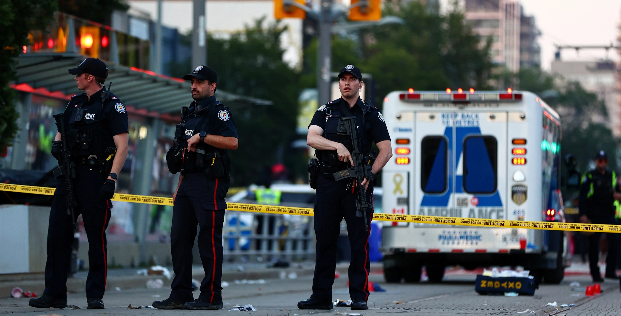 Toronto police officers at the scene of a shooting on St. Clair Avenue with police tape and emergency vehicles present.