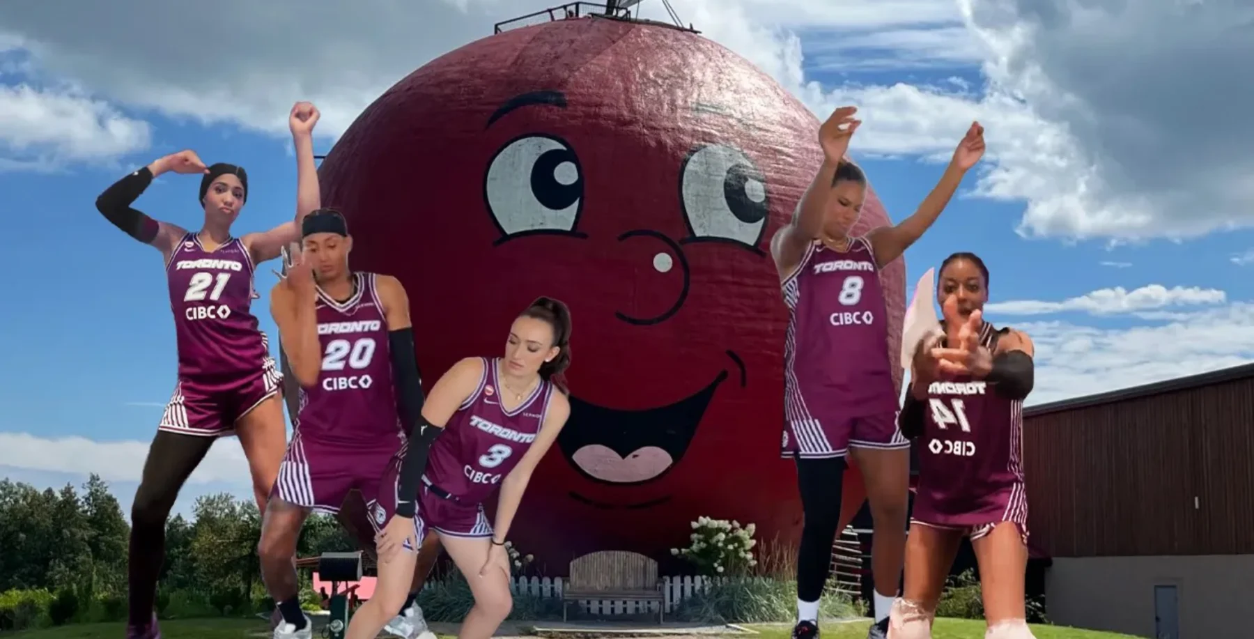 Five women in purple basketball uniforms pose in front of a giant smiling apple sculpture outdoors on a sunny day.
