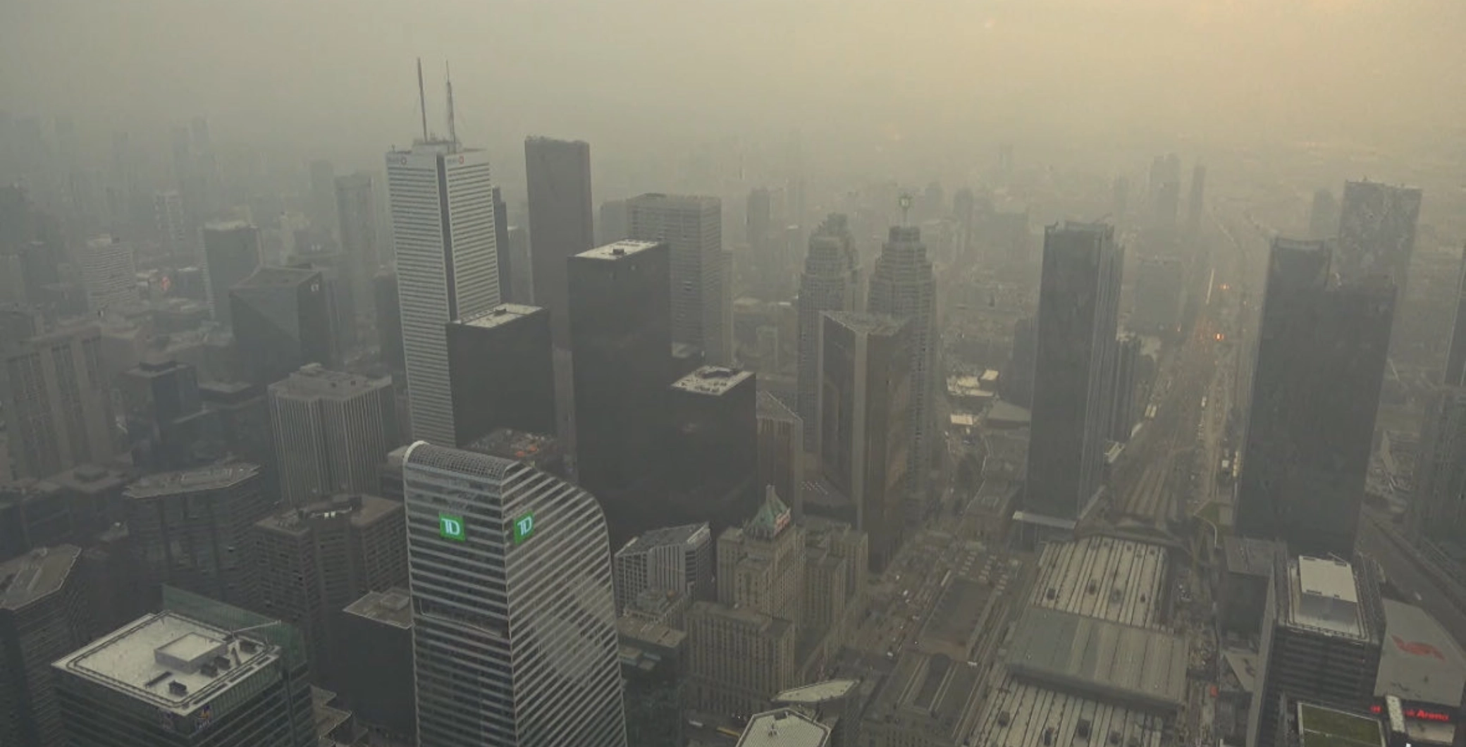Toronto skyline obscured by smoky haze from Ontario wildfires, with skyscrapers barely visible through the air pollution.