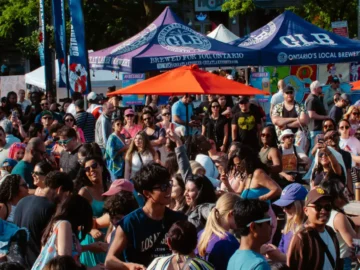 A lively outdoor event in Toronto with a large crowd, colorful tents, and orange umbrellas, showcasing community gathering, local breweries, and city entertainment in a vibrant urban setting.