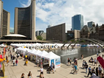 Crowd enjoying outdoor art fair at Toronto waterfront with city skyline in the background.