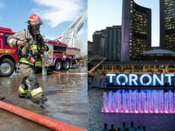 Firefighter in protective gear spraying water at a fire truck near Toronto's city skyline and illuminated fountain.